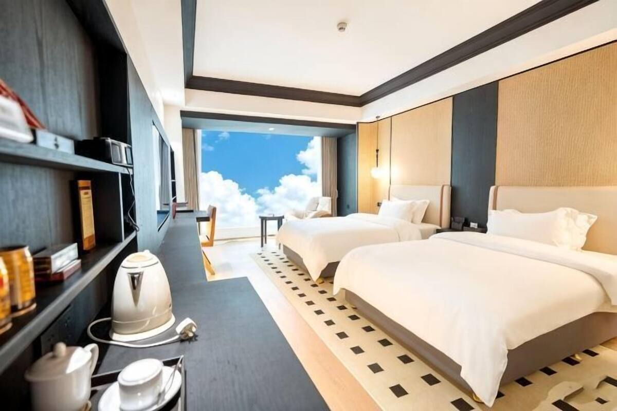 Habitación de hotel con dos camas, cafetera, estantería y vista al cielo.