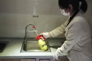 A person wearing gloves using a spray bottle in a kitchen sink.