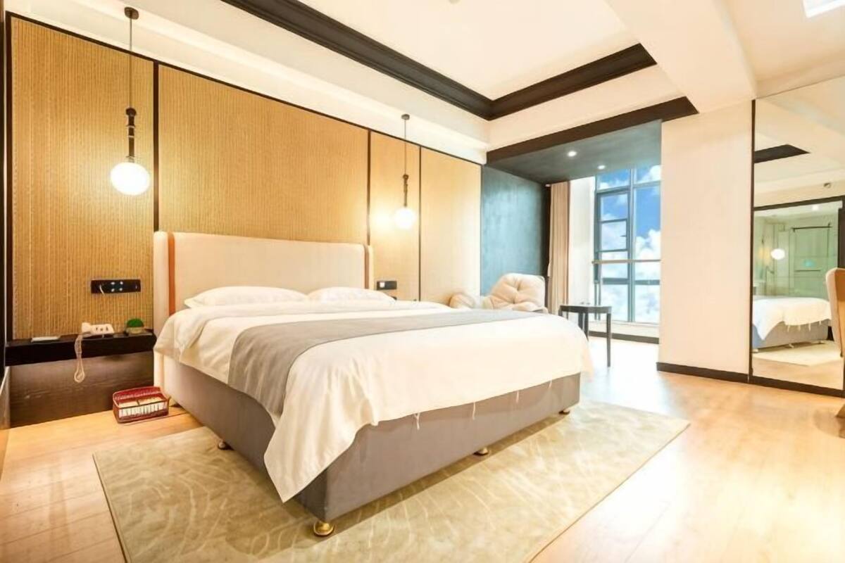 Un dormitorio moderno con una cama grande, mesitas de noche y vistas de la ciudad a través de amplios ventanales.
