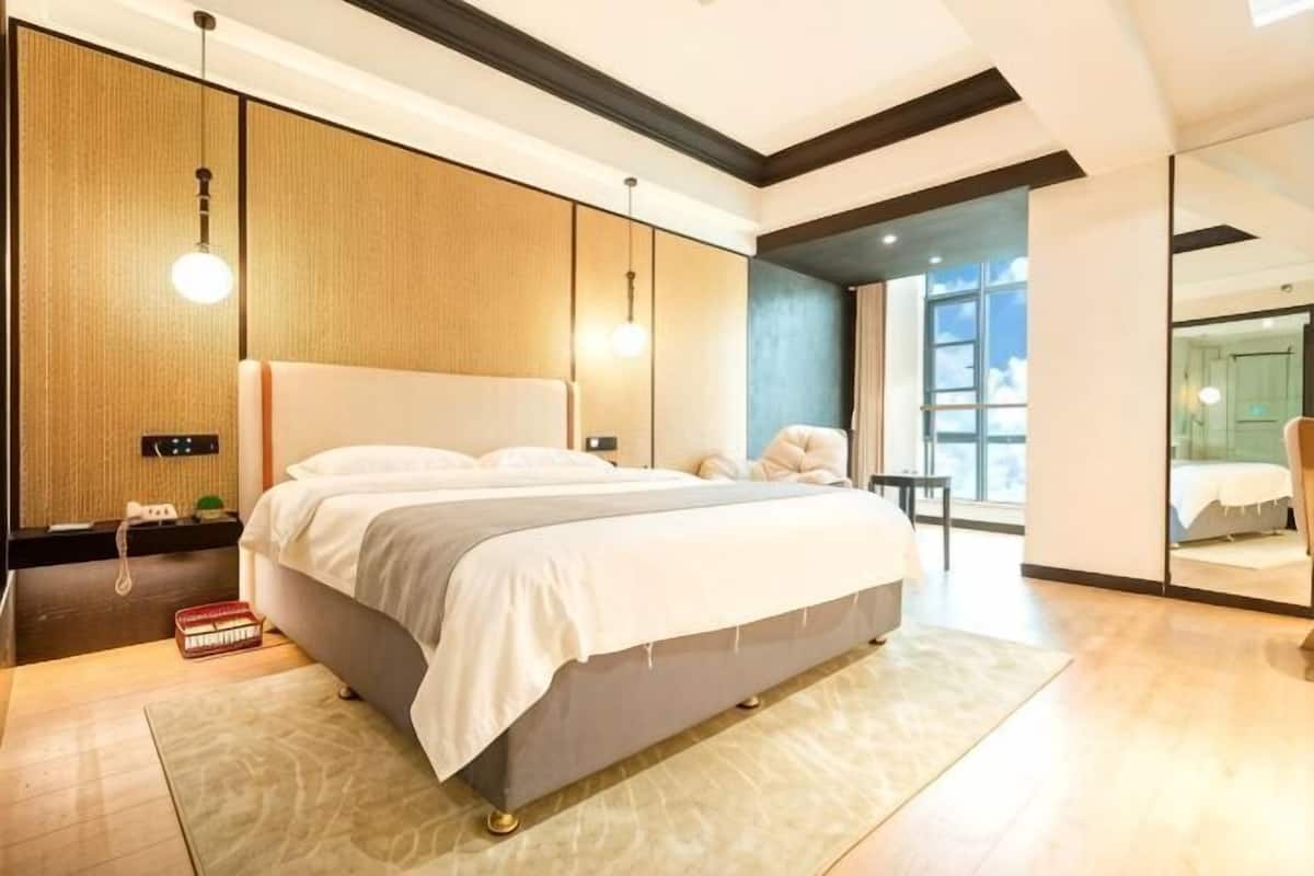 A modern bedroom with a large bed, bedside tables, a nightstand, and a view of the city through large windows.