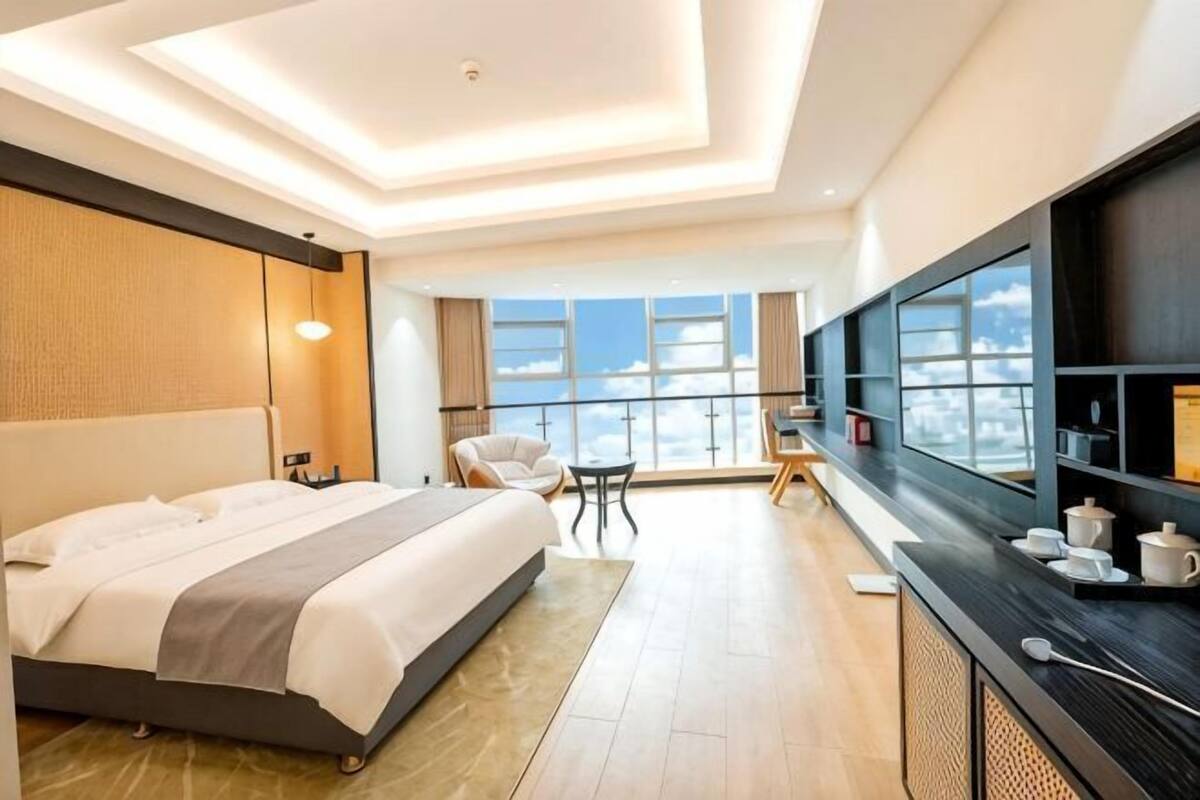 Una habitación de hotel moderna con una cama grande, un escritorio, una silla y vistas al cielo a través de un ventanal amplio.
