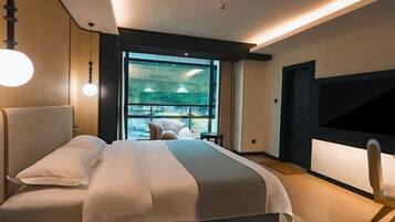 A modern hotel room with a large bed, a TV, and a view of a cityscape through the window.