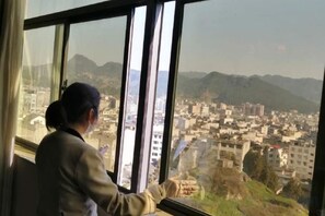 Una persona sentada junto a una ventana con vista a un paisaje urbano que incluye edificios y montañas.