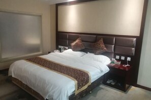 A hotel room with a large bed, a nightstand with a phone and a lamp, and a shoe rack.