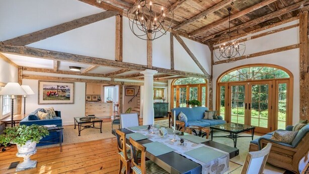 Una habitación amplia con vigas de madera, una mesa de comedor con sillas, un sofá y un ventanal con vistas al verdor.