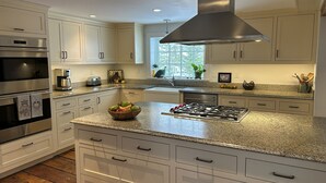 Cocina moderna con armarios blancos, electrodomésticos de acero inoxidable, encimera de granito y una isla central con estufa a gas.