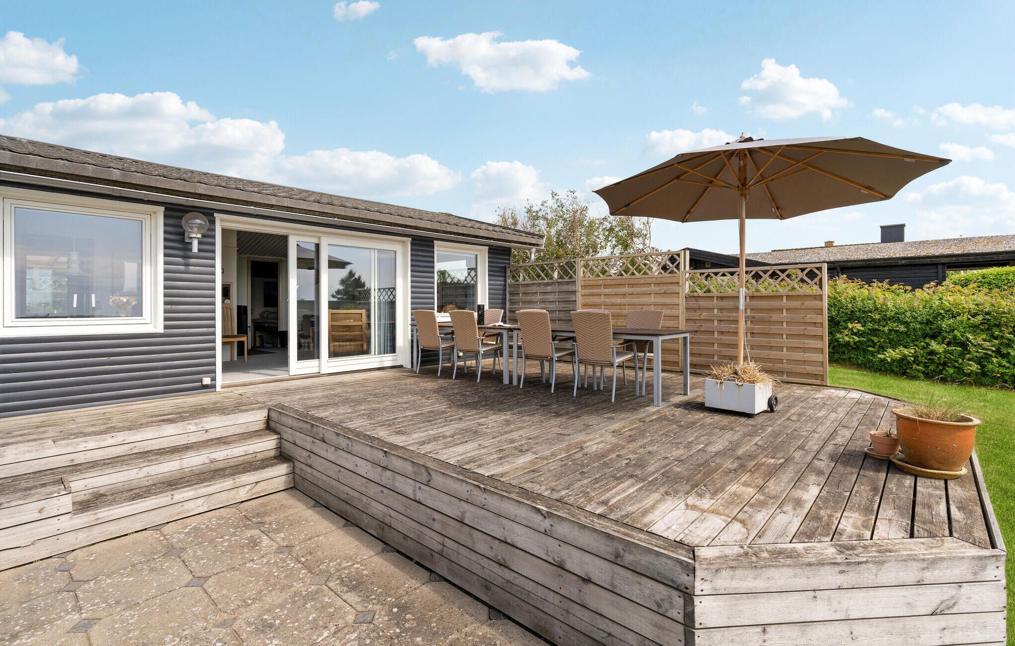 Eine Holzterrasse mit Gartenmöbeln und einem großen Sonnenschirm.