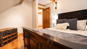 Une chambre à coucher avec une tête de lit en bois, un lit avec une literie à motifs, une table de chevet avec une lampe et une commode en bois.