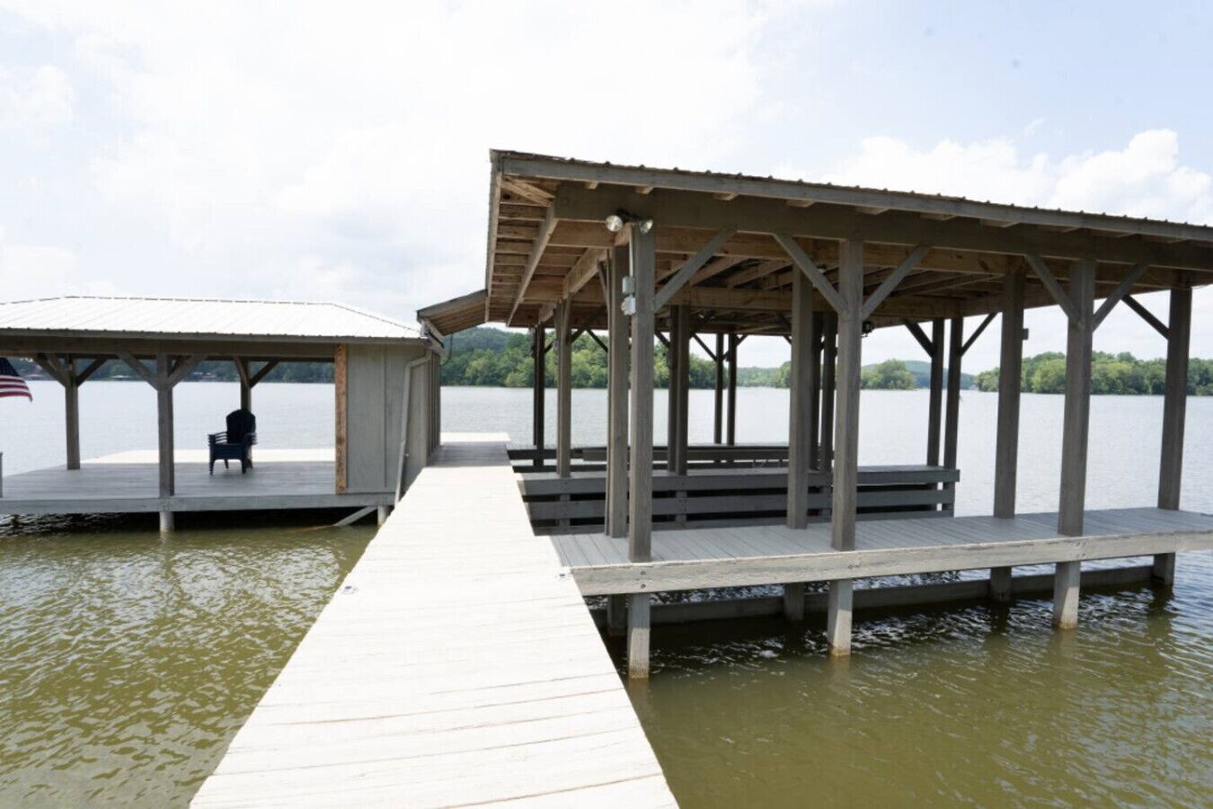A wooden pier leading to a covered dock with a bench and an American flag.