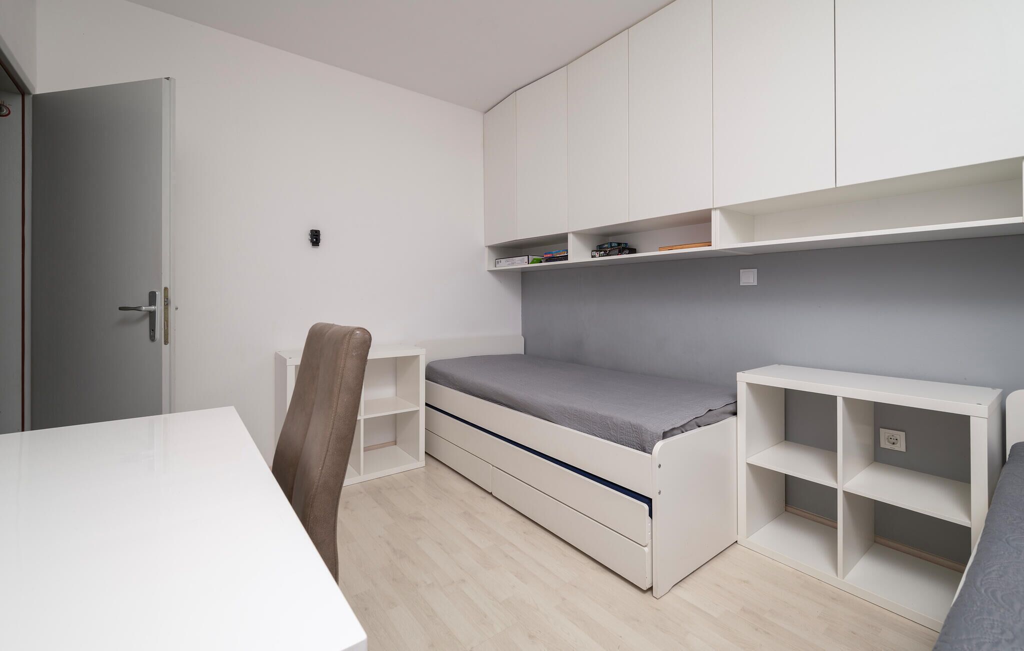 A minimalist bedroom with a bed, a desk, and built-in shelving.