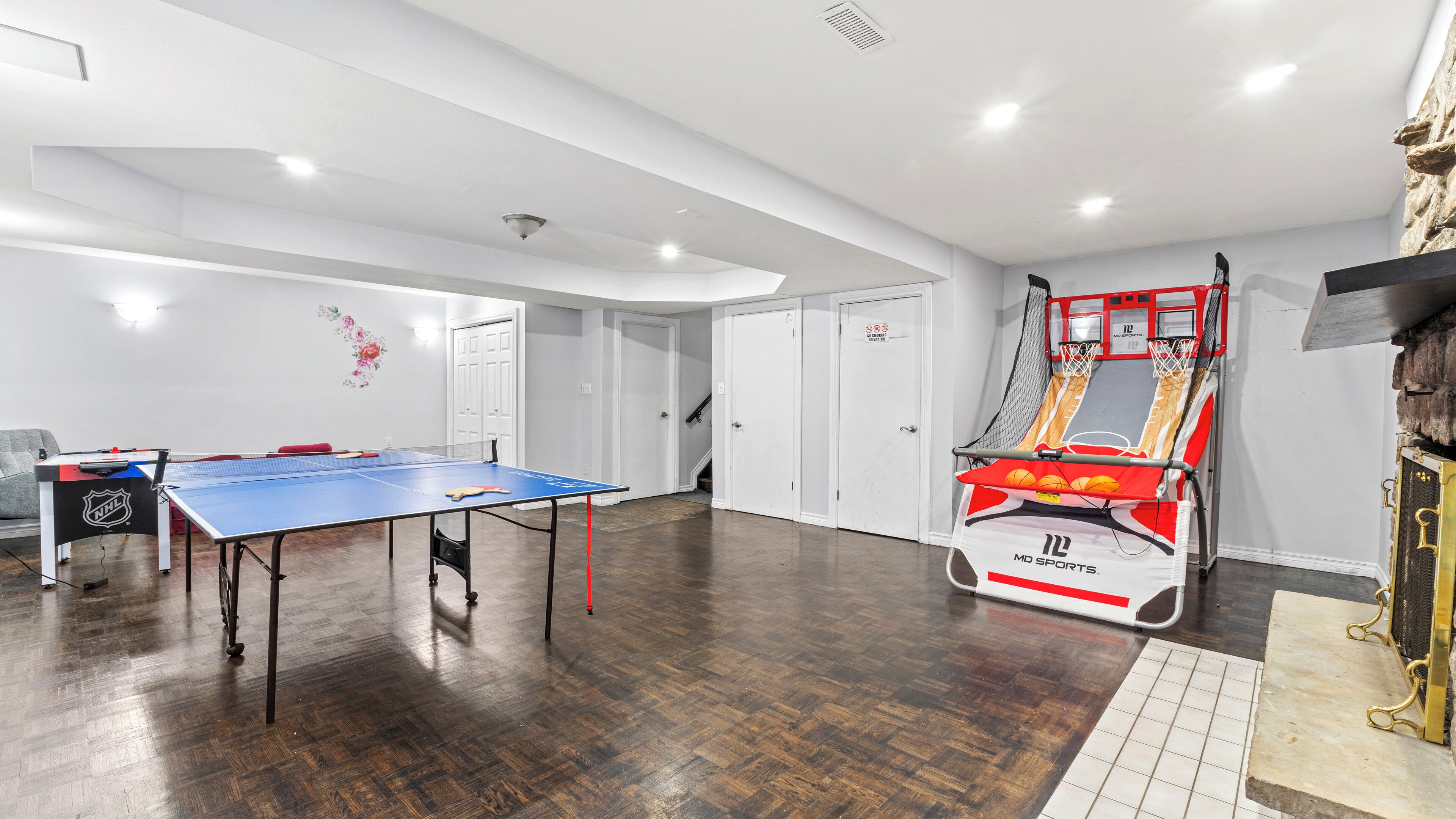 Een ruime kamer met een tafeltennistafel, een basketbal-arcade en een deur die naar een andere kamer leidt.