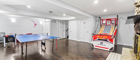 Een ruime kamer met een tafeltennistafel, een basketbal-arcade en een deur die naar een andere kamer leidt.