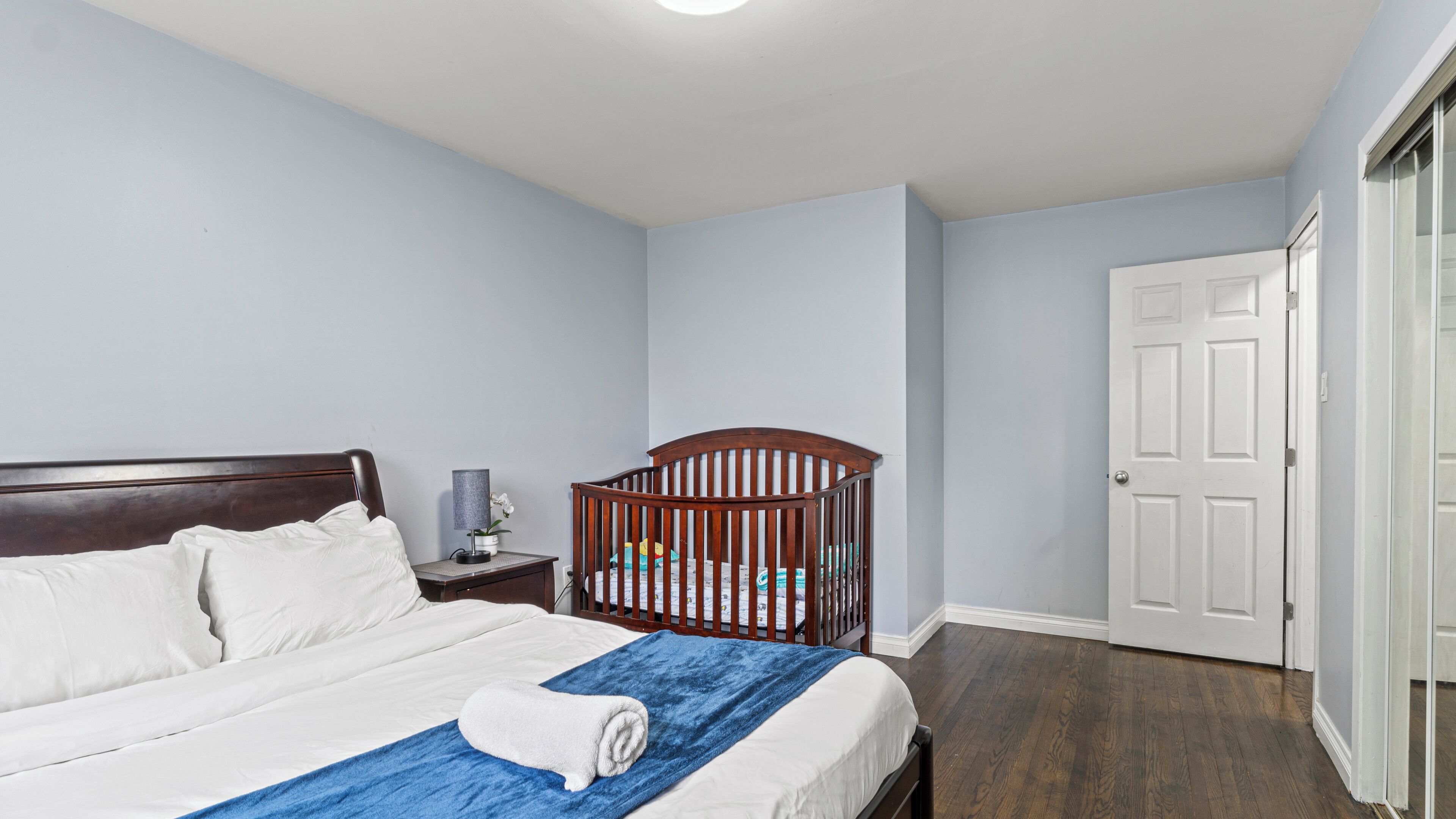 Quarto com cama, berço, mesa de cabeceira, abajur e porta.