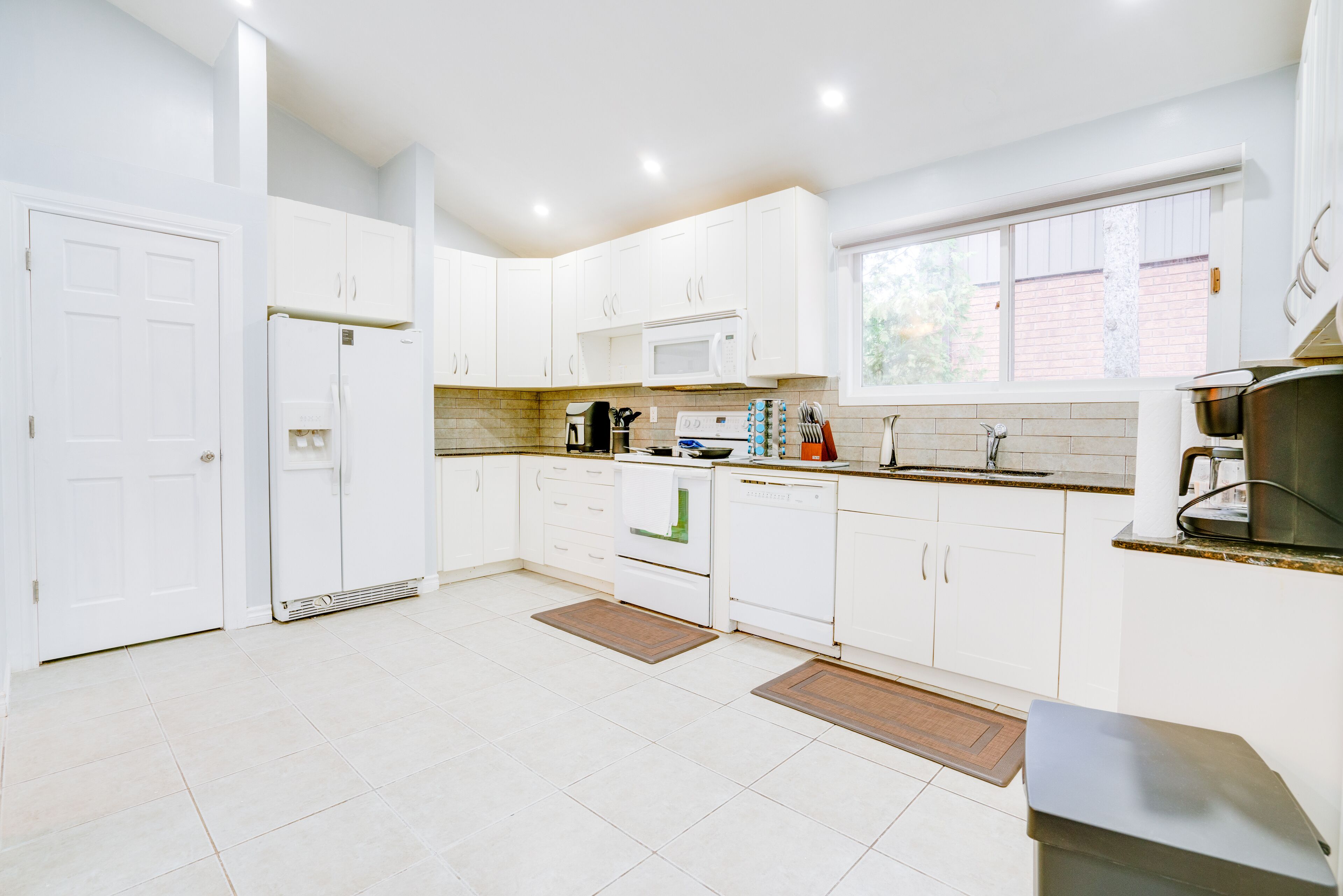 A modern kitchen with white cabinets, a microwave, a coffee maker, and a window providing natural light.