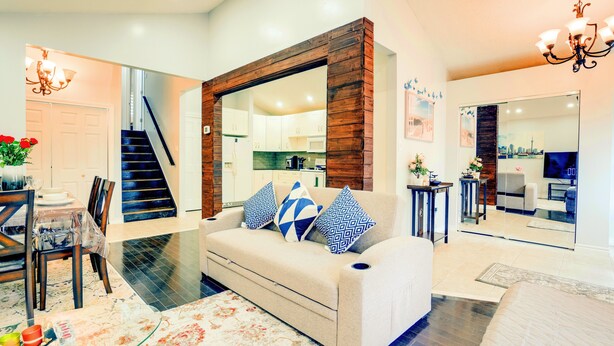 A modern living room with a sofa, coffee table, and a dining area with chairs and a table. - Furnished Family Home ★ KING BED ★ Parking ★ BBQ ★ Backyard ★ Discounted Price (Pickering)