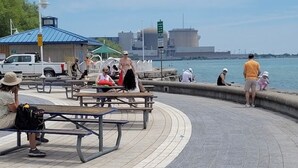 A waterfront promenade with benches and picnic tables, a clear sky, and a distant industrial skyline. - Furnished Family Home ★ KING BED ★ Parking ★ BBQ ★ Backyard ★ Discounted Price (Pickering)