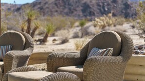 Two wicker chairs with cushions, positioned outdoors with a desert landscape and mountains in the background.