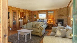 A cozy room with a bed, a sofa, a small table, a fireplace, and wooden paneling.