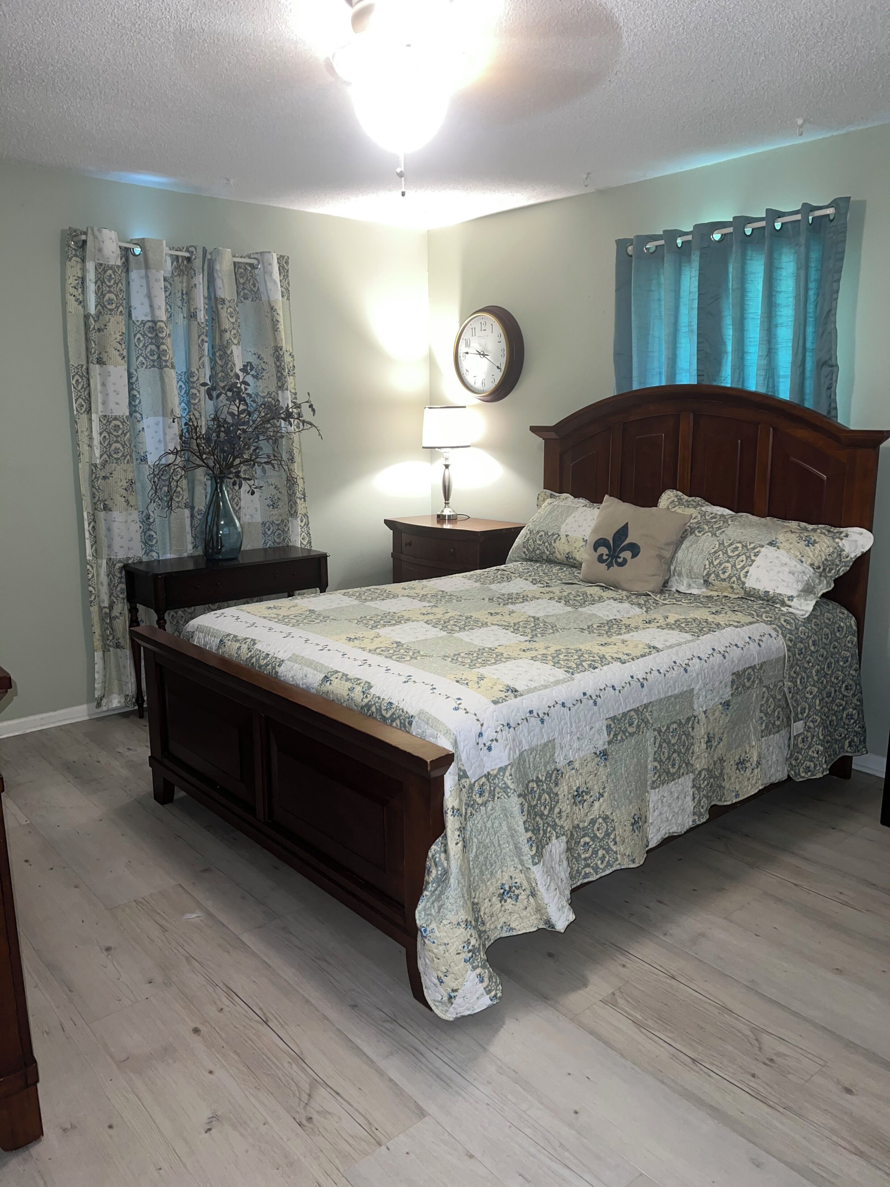 A bedroom with a wooden bed, a nightstand, a wall clock, and a lamp.
