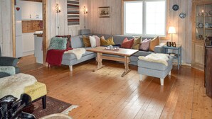 A cozy living room with a sofa, a coffee table, and a small side table. There is a window with blinds, a refrigerator, and a cabinet with dishes. - Awesome home in Ustaoset with WiFi (Ustaoset)