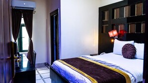 A hotel room with a large bed, a bedside table, a desk, and a window with curtains. - Where Elegance, Comfort, and Prestige Meet. (Delta)