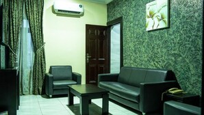 A living room with a sofa, two armchairs, a coffee table, a TV, an air conditioner, a door, and a wall with a floral painting. - Where Elegance, Comfort, and Prestige Meet. (Delta)