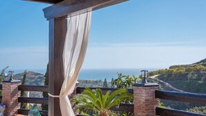 A balcony with a view of the ocean, a wooden pergola, and a brick railing.