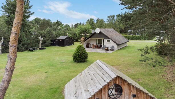 A rustic cabin with a thatched roof, surrounded by a grassy yard and dense trees. - 2 bedroom stunning home in Rødby (Rødby)