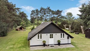 A small, single-story house with a sloped roof, surrounded by a grassy lawn and trees. - 2 bedroom stunning home in Rødby (Rødby)