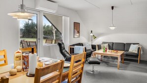 A modern living room with a dining area, a sofa set, and a coffee table. There is a large window providing a view of the outdoors. - 2 bedroom stunning home in Rødby (Rødby)