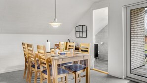 A dining area with a wooden table and chairs, a hanging light fixture, and a view of the outside through a glass door. - 2 bedroom stunning home in Rødby (Rødby)
