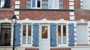 A building with a white door, blue shutters, and a brick facade. - Bay view house in the heart of the Abbaye district (Saint-Valery-sur-Somme)