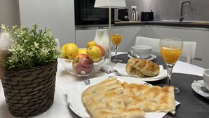 Une table de petit-déjeuner avec des fruits, un croissant et des boissons, dans une cuisine moderne.