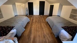 Une petite chambre mansardée de forme triangulaire, avec deux lits simples, un ventilateur de plafond et un plancher en bois.
