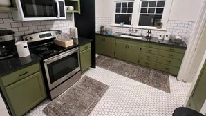 Une cuisine avec des meubles de couleur verte, un four à micro-ondes, une cuisinière et une fenêtre au-dessus de laquelle est accrochée une enseigne.