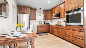 Une cuisine moderne avec des meubles en bois, des appareils électroménagers en acier inoxydable et un coin repas comprenant une table en bois et des sets de table.