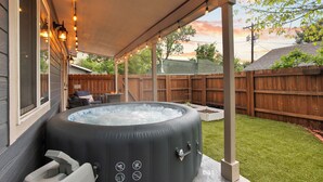 Un bain à remous sous une terrasse couverte, avec une clôture en bois en arrière-plan.