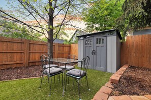 A backyard with a wooden fence, a metal table with chairs, and a shed. - Luxury Downtown Cottage w/ Hot Tub, Private Yard, Fireplace & Fire Pit (Colorado Springs)