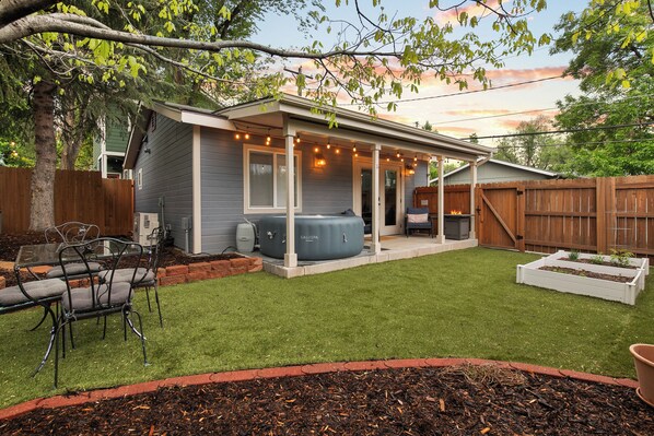 A backyard with a covered patio, a hot tub, and a wooden fence. - Luxury Downtown Cottage w/ Hot Tub, Private Yard, Fireplace & Fire Pit (Colorado Springs)