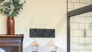 Une salle de bain avec deux peignoirs blancs suspendus à un porte-serviettes, un meuble en bois contenant des serviettes et une plante en pot.