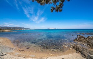 Une plage bordée d’une eau turquoise et limpide, d’une côte rocheuse et de montagnes lointaines.