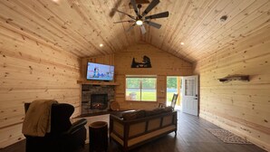 A cozy log cabin interior with a fireplace, a television, and a ceiling fan.