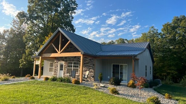 A two-story house with a stone facade, a covered porch, and a metal roof.