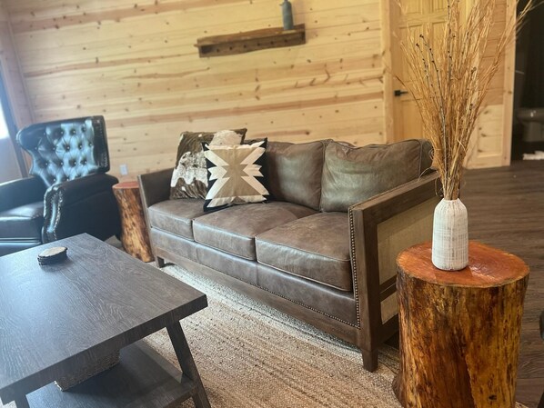 A cozy living room with a leather sofa, a wooden coffee table, and a rustic wooden floor.