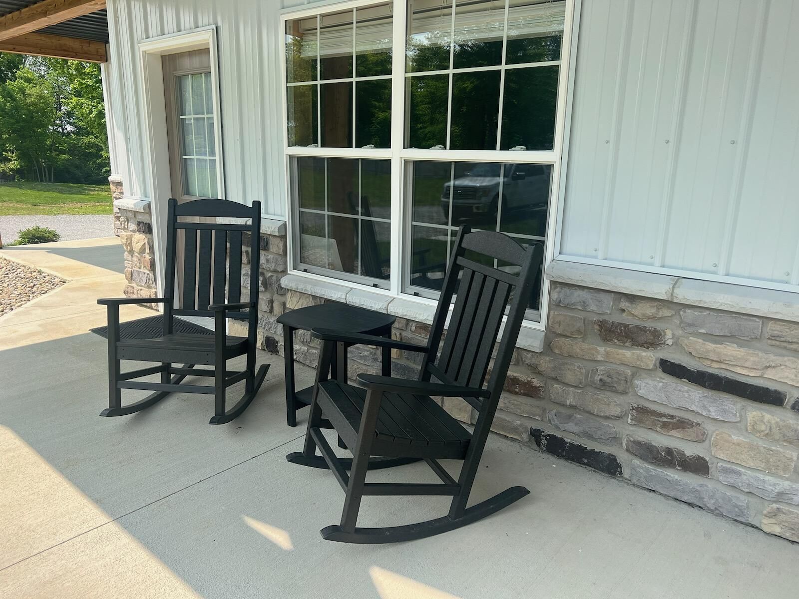 Une terrasse avec deux fauteuils à bascule et une petite table, située à côté d’un bâtiment aux murs en pierre et aux grandes fenêtres.
