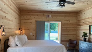 A wooden cabin room with a bed, a ceiling fan, an exit sign, and a view through a door.