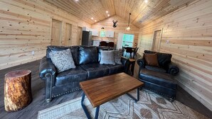 A log cabin interior with a leather sofa, a wooden coffee table, and a dining area with a table and chairs.