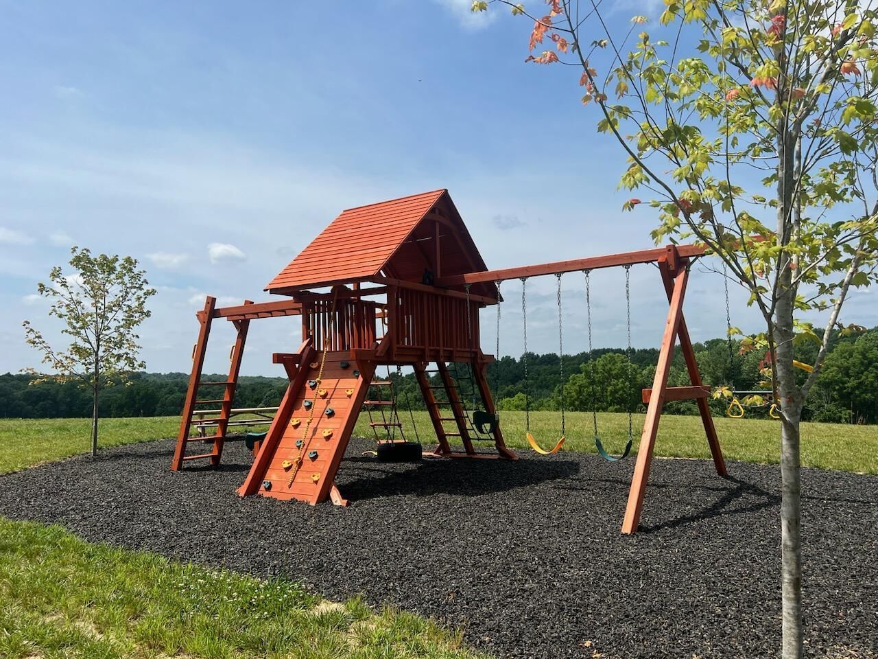 Un’area giochi in legno con scivolo e altalene su fondo di ghiaia.