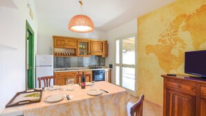 Une cuisine avec des meubles de rangement en bois, une table à manger dressée pour deux personnes et un téléviseur posé sur un meuble en bois.