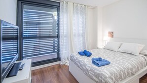 Hotellihuone, jossa on sänky, työpöytä, televisio ja ikkuna, jossa on sälekaihtimet.